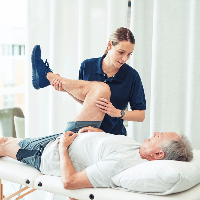 Female massage therapist stretches an older male who is laying on a massage table, she pushes his knee toward his chest