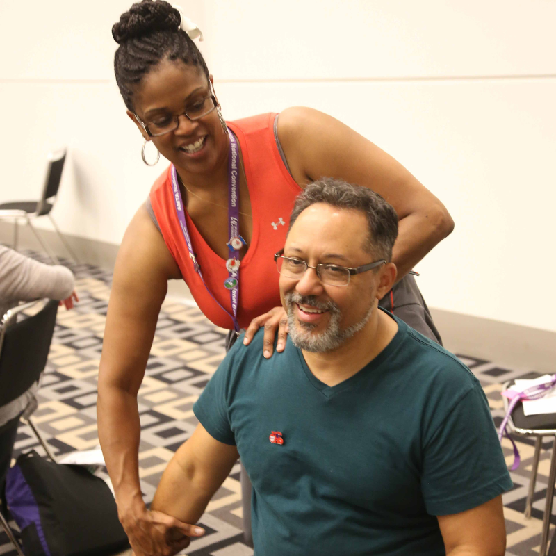 Smiling woman practices massage therapy on a man who is sitting down