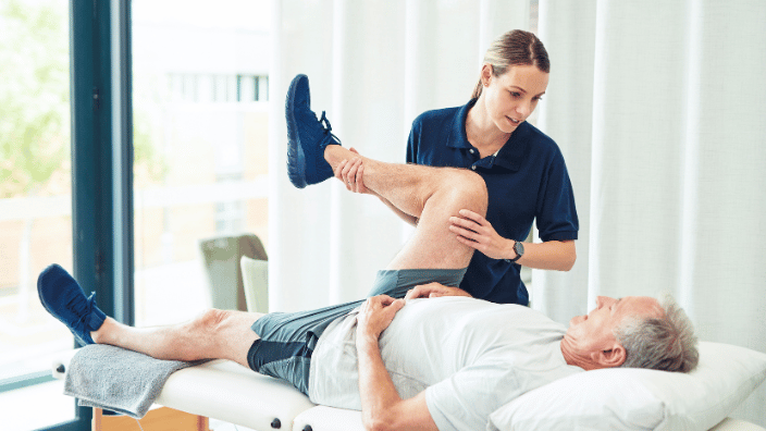 Image of young woman stretching an older man as he lays on a massage table.