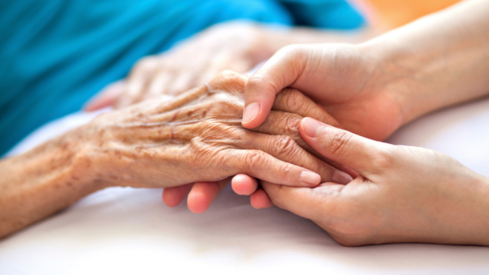 A massage therapist holds an elderly individual's hand in both of theirs